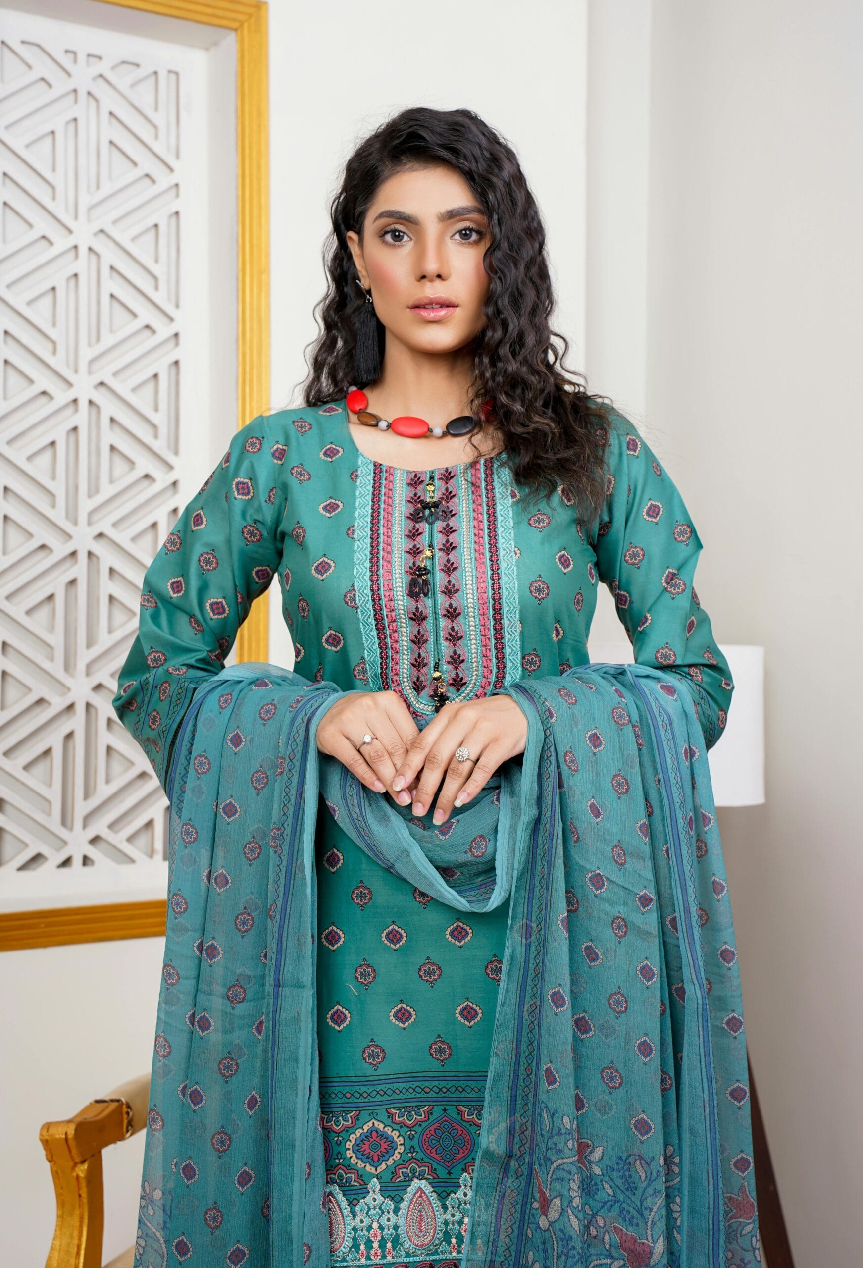 Woman in green embroidered dress with shawl in stylish indoor setting.
