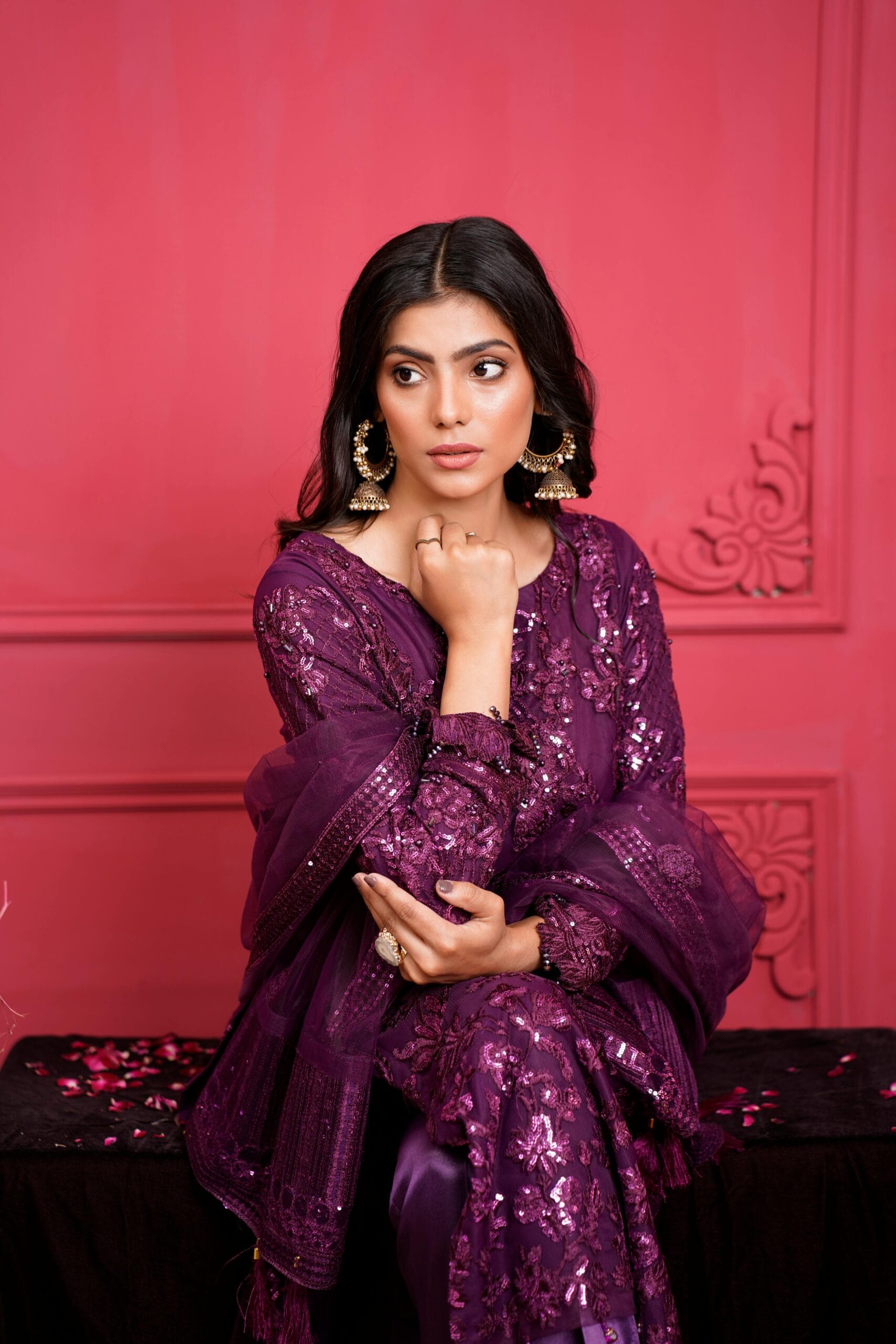 Portrait of a woman in an embroidered purple dress with elegant jewelry sitting indoors.