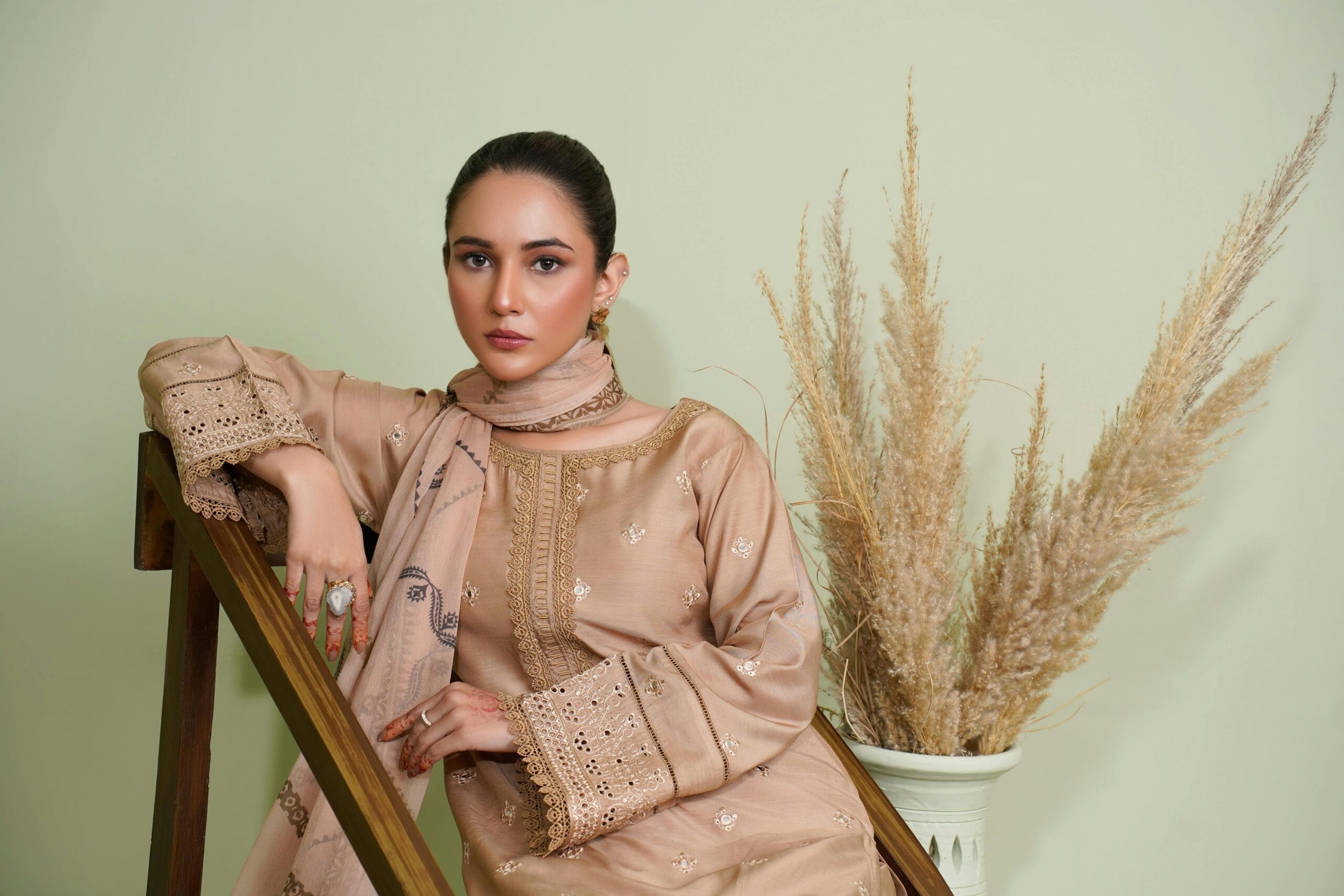 A stylish woman wearing an embroidered dress in an indoor setting, embodying elegance and cultural fashion.